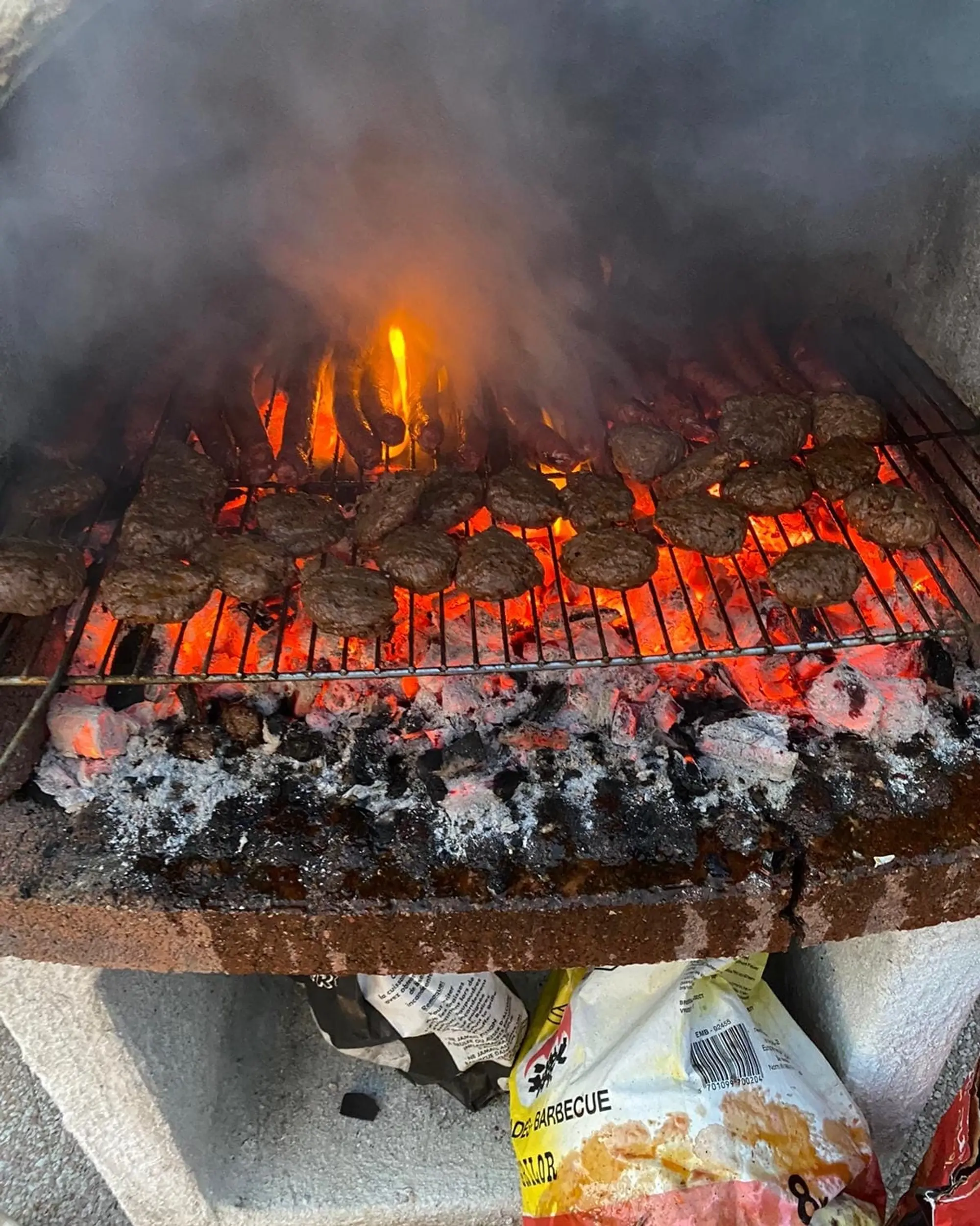 Steaks hachés et viandes grillant sur un barbecue au charbon, flammes et fumée