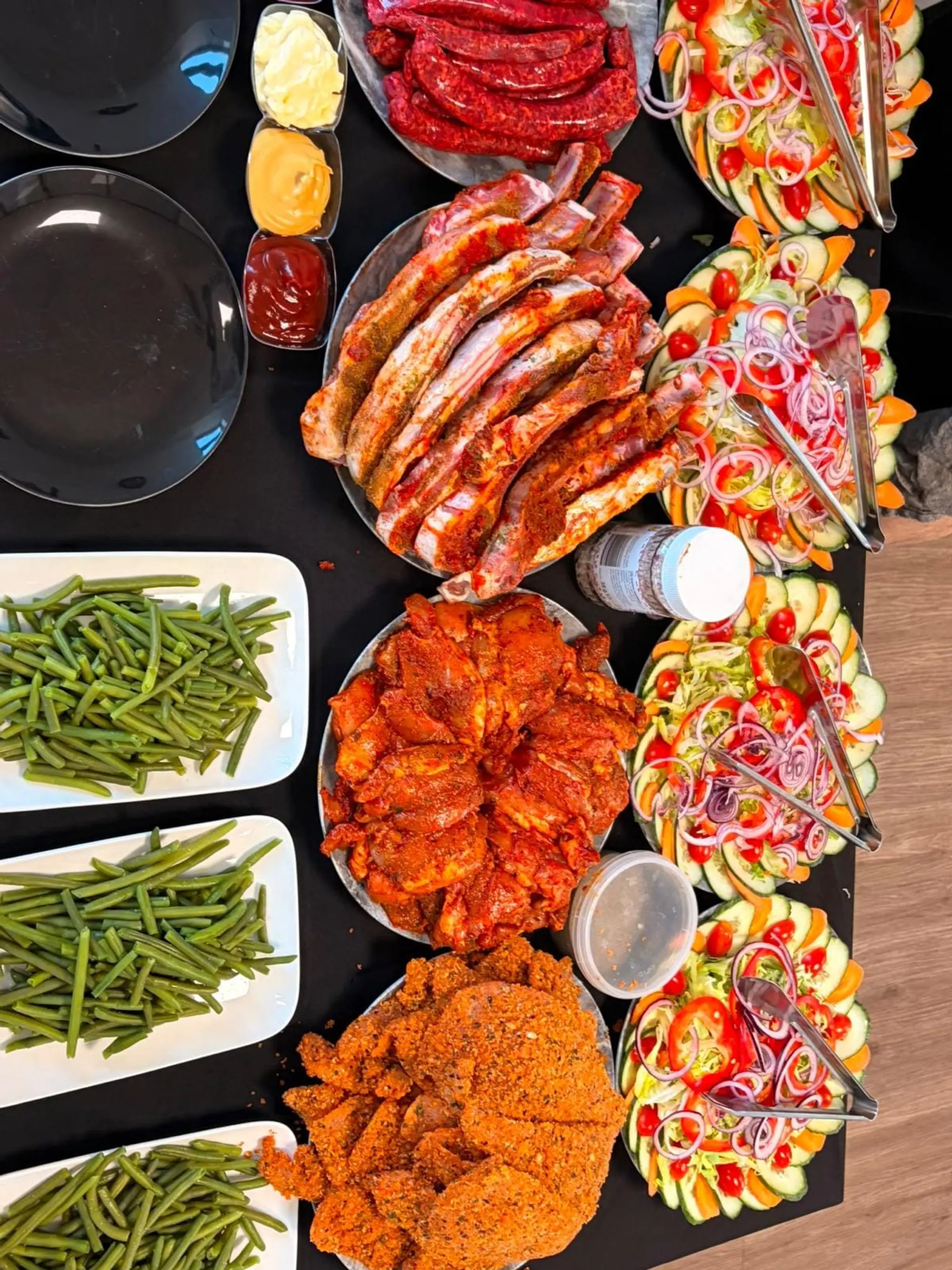 Vue du dessus d’un buffet : haricots verts, côtes marinées, poulet épicé, schnitzels, merguez et salades composées