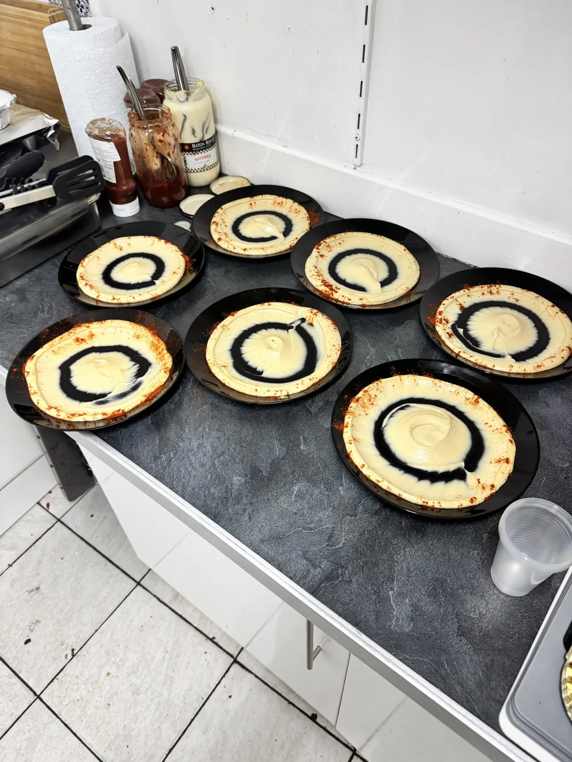 Galettes rondes garnies de viande hachée et d’un filet de sauce, posées sur des plateaux noirs