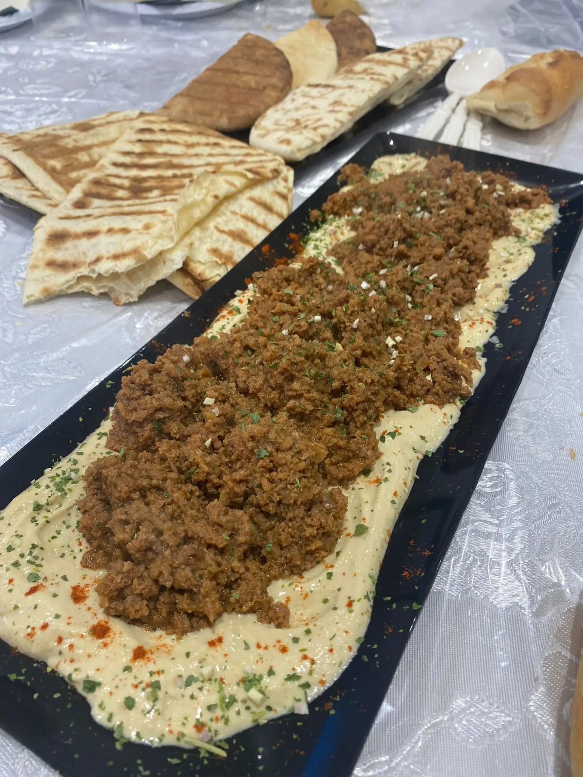 Grand plateau de houmous garni de viande hachée, pains grillés à côté