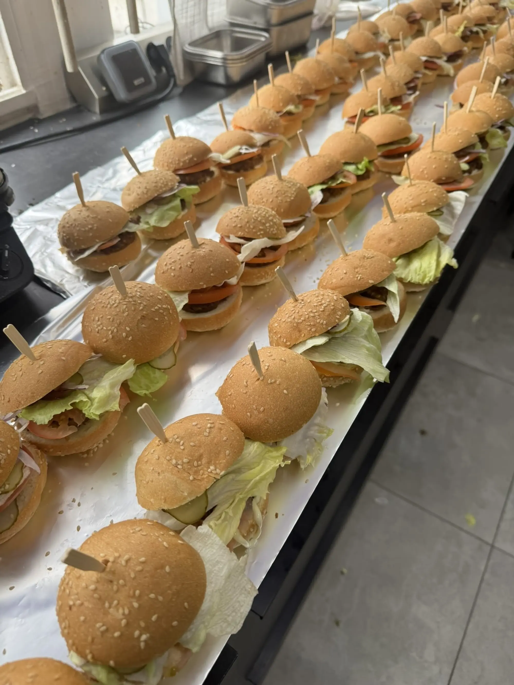 Rangées de mini-burgers au sésame piqués d’un pic en bois, prêts à servir