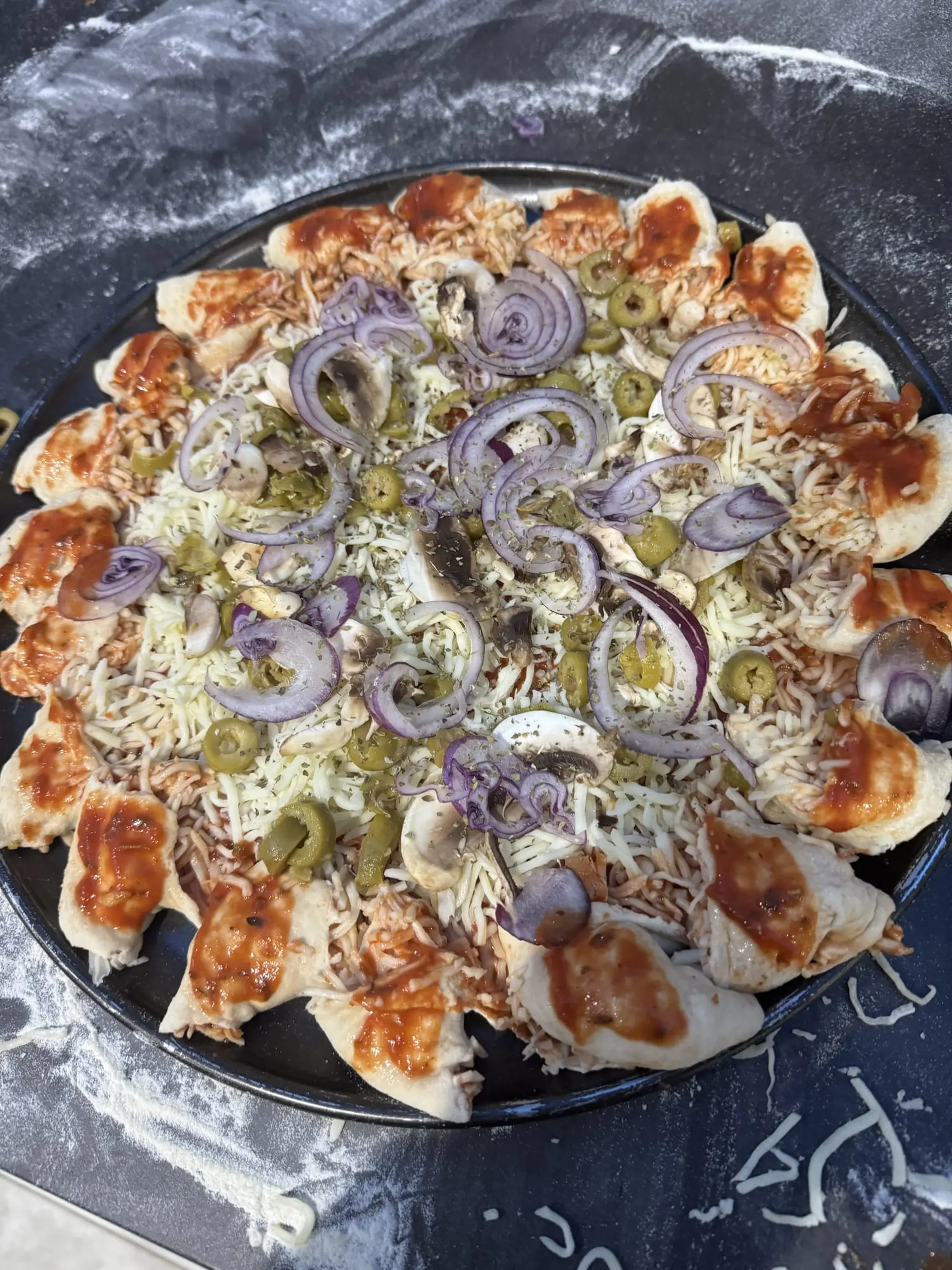Pizza garnie d’oignons rouges et d’olives vertes, sur une plaque noire