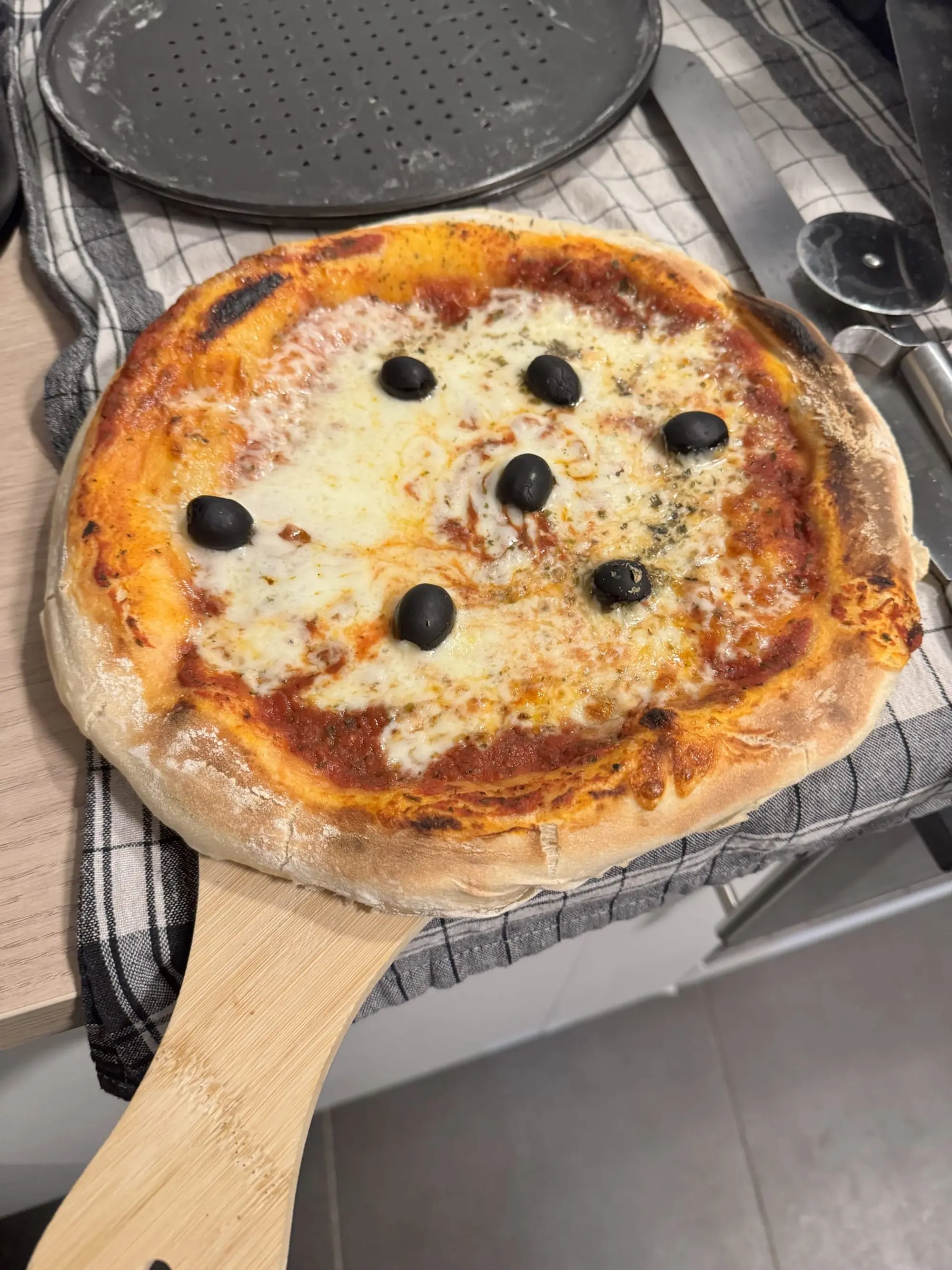 Pizza au fromage et aux olives noires, tout juste sortie du four, posée sur une pelle en bois