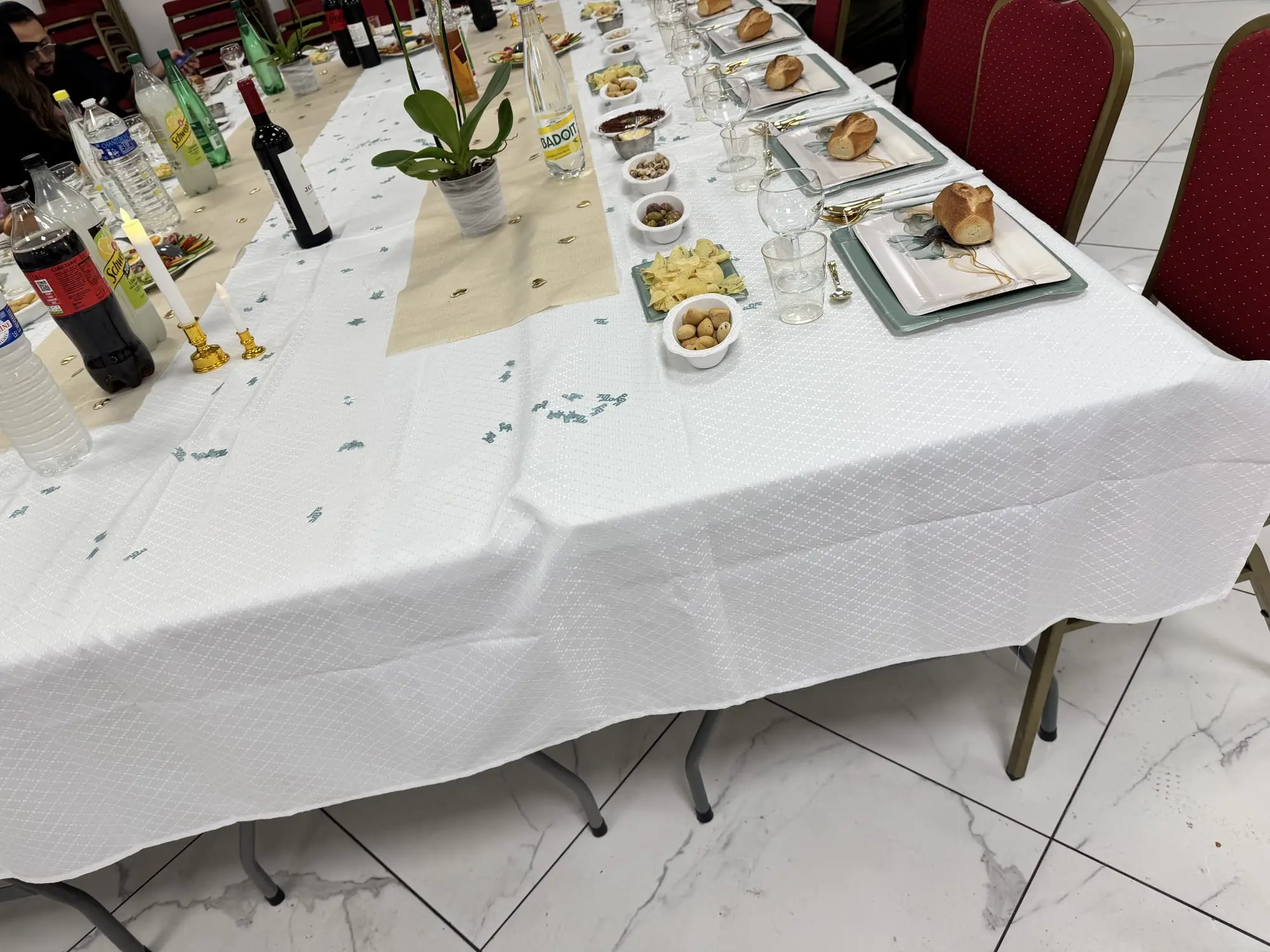 Gros plan sur une table de réception : nappe blanche, chemin de table doré, petits pains et coupelles de salades